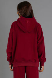 A person stands facing away, wearing the Maroon Panache Hooded Sweatshirt and matching pants from the Panache Apparel Collection against a plain gray background.