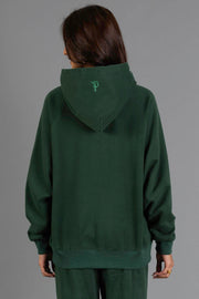 A person with long brown hair, facing away from the camera, is wearing the Panache Apparel Collection’s Dark Green Panache Hooded Sweatshirt and matching pants. The sweatshirt features a small embroidered letter “P” on the back of the hood. The background is plain gray.