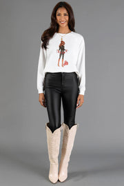 A woman wears a lightweight Panache Apparel Collection Merry Season Sweatshirt featuring a woman holding a MERRY banner, paired with black leggings and tall light-colored boots.