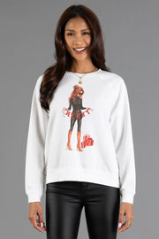 Woman wearing a white long-sleeve Merry Season Sweatshirt by Panache Apparel Collection, featuring an illustration of a woman holding a MERRY banner with gift boxes nearby.