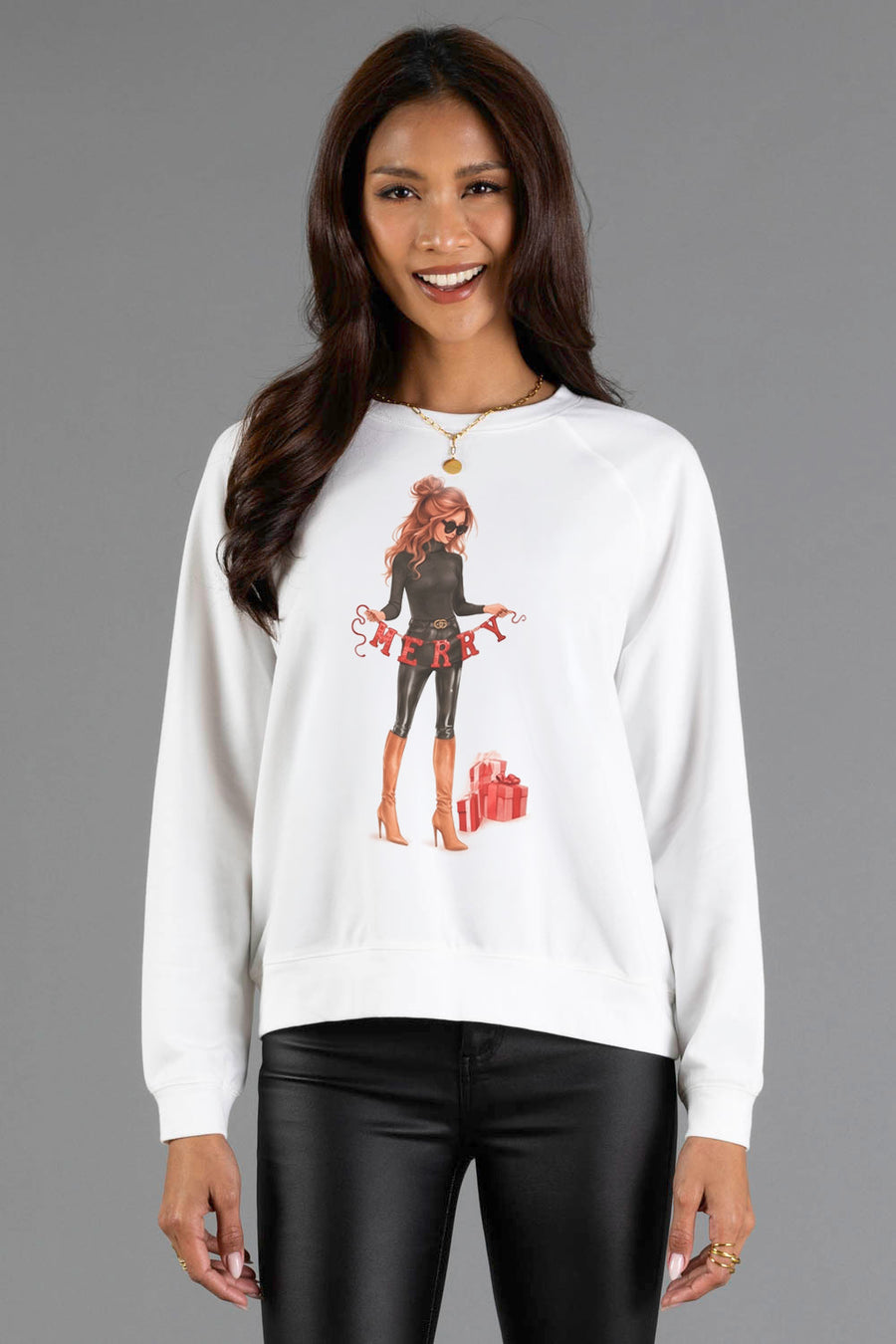 Woman wearing a white long-sleeve Merry Season Sweatshirt by Panache Apparel Collection, featuring an illustration of a woman holding a MERRY banner with gift boxes nearby.