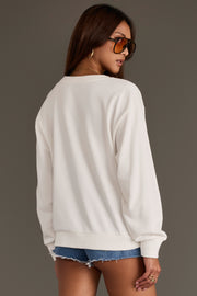 A woman wearing the Born to Be Wild Sweatshirt from Panache Apparel Collection, paired with denim shorts, sunglasses, and jewelry, stands with her back to the camera against a plain background.