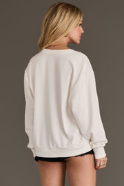 A woman with blonde hair stands facing away from the camera, showcasing the back of her Panache Apparel Collection “Outlaw State of Mind” sweatshirt and black shorts against a plain gray background.