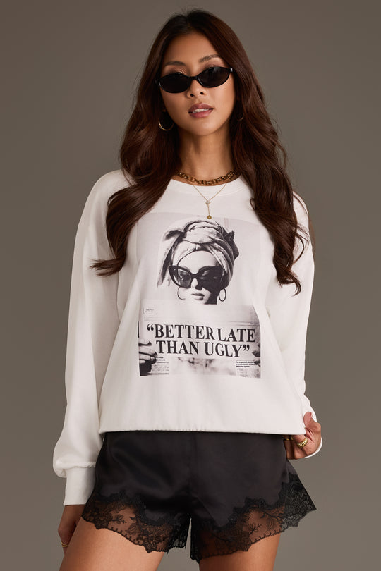 A woman poses confidently against a plain background, wearing sunglasses, black lace-trimmed shorts, and the Panache Apparel Collection’s “Better Late Than Ugly” graphic sweatshirt.