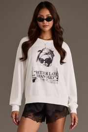 A woman wears the Panache Apparel Collection “Better Late Than Ugly” Sweatshirt, featuring a graphic print of a woman and bold text, paired with black lace shorts and sunglasses, as she stands against a plain background.