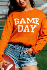 A woman stands on a sports field holding a football, dressed in the Panache Apparel Collection Orange Game Day Sweater with denim shorts for a relaxed, vibrant look.