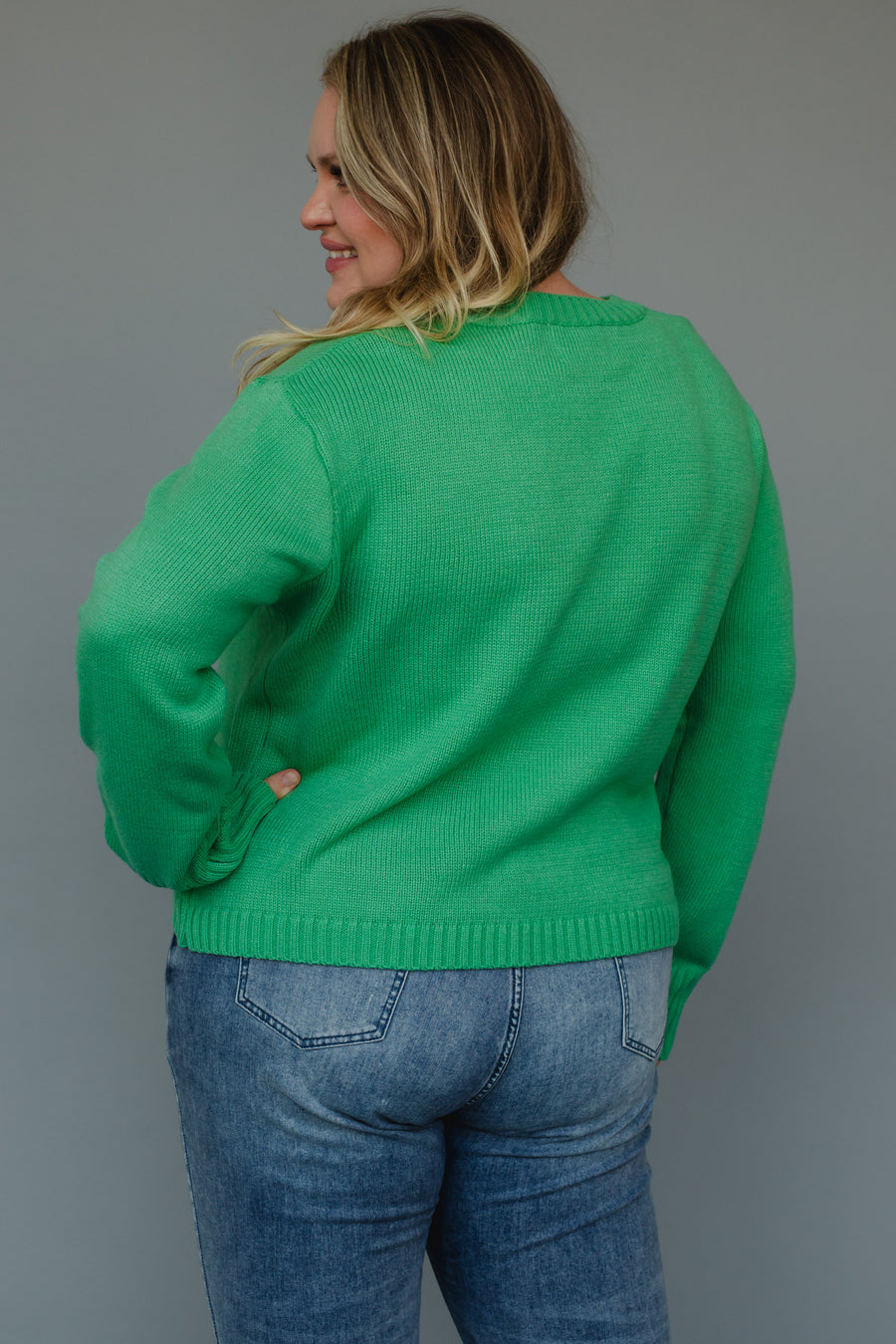 A person wearing a relaxed fit, bright mint green Mint Merry Sweater and blue jeans.