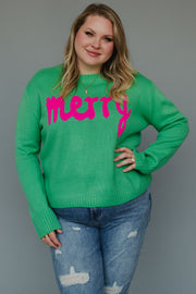 A woman wearing a Mint Merry Sweater in mint green with the word merry in pink script, paired with distressed blue jeans.