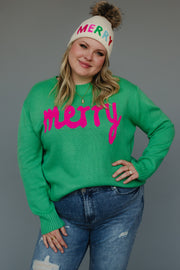 A person wears a Mint Merry Sweater in mint green with the word merry in pink, paired with a cream-colored knit beanie that has MERRY in colorful letters and a faux-fur pom-pom.