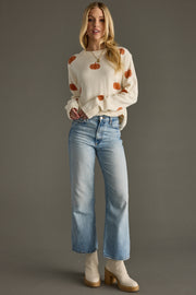Full-length model styling Panache Apparel’s ivory fall pumpkin sweater with jeans and ankle boots.