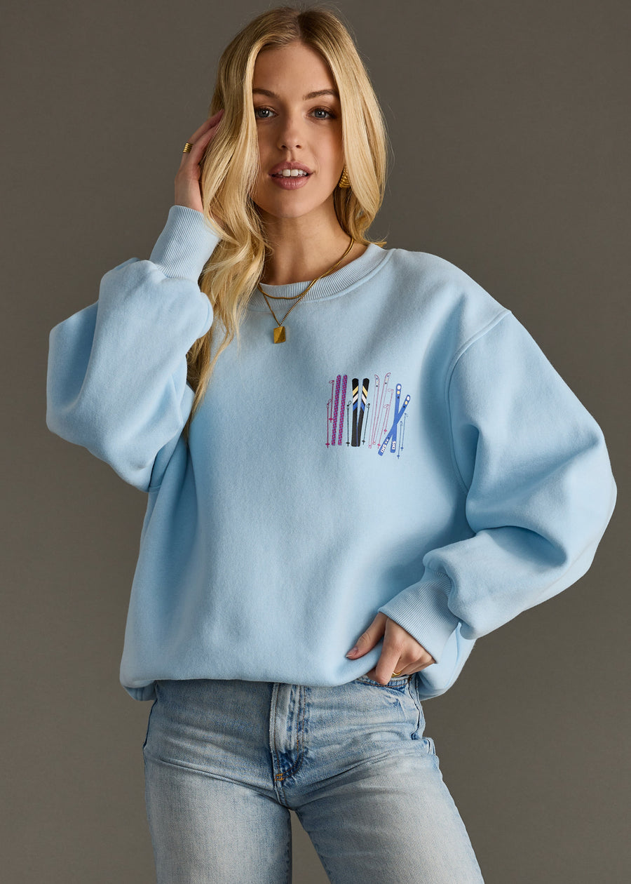 Woman wearing a light blue sweatshirt with a colorful design on the chest against a gray background
