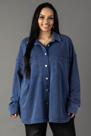 A woman with long dark hair smiles while wearing the Panache Apparel Collection's Dark Blue Washed Soft Button Up, styled oversized with large front pockets and black pants, standing against a plain gray background.