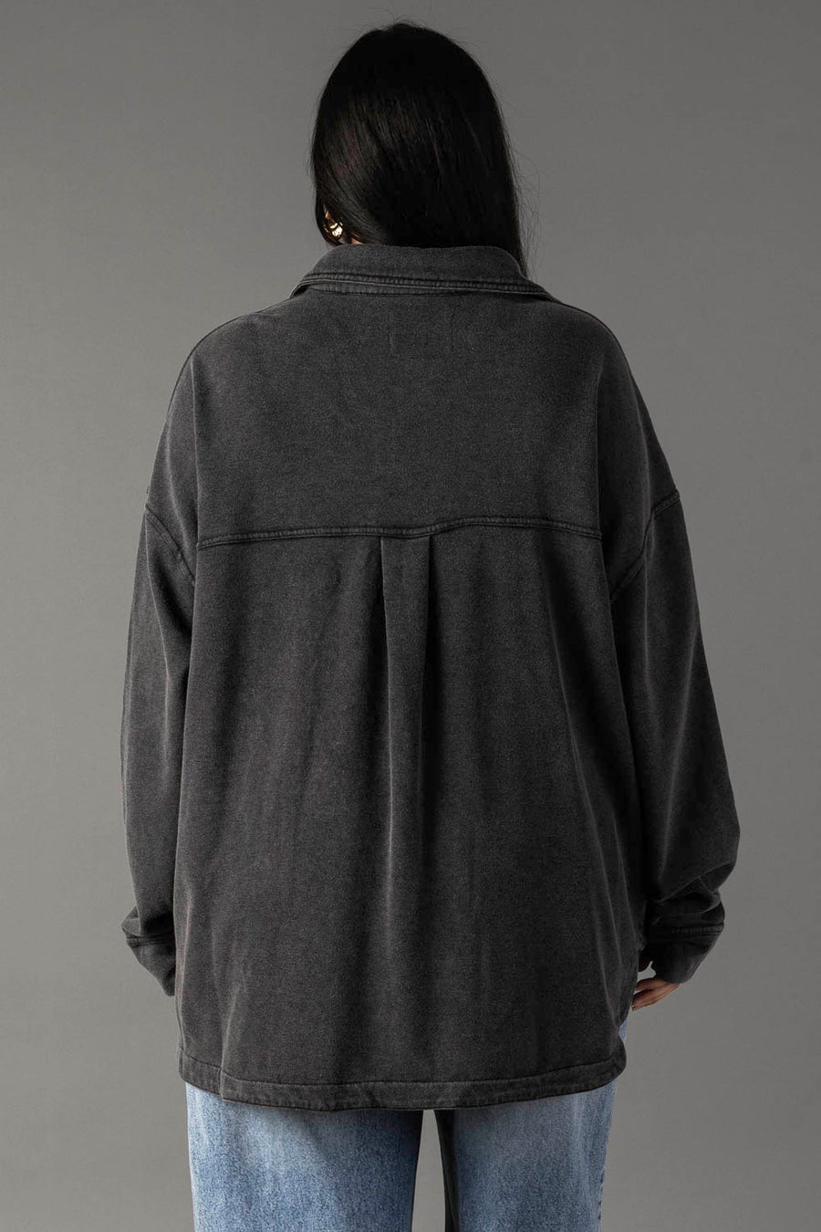A person with long dark hair stands with their back to the camera, wearing Panache Apparel Collection's Black Washed Soft Button Up and light blue jeans against a plain gray background.