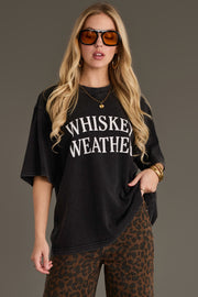 A woman with long blonde hair wears sunglasses, hoop earrings, the Panache Apparel Collection Black Whiskey Weather Tee, and leopard print pants, posing against a plain background.