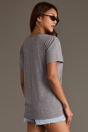 A person wearing a relaxed fit Gray Wine Tee with a center back seam and light-wash denim shorts.