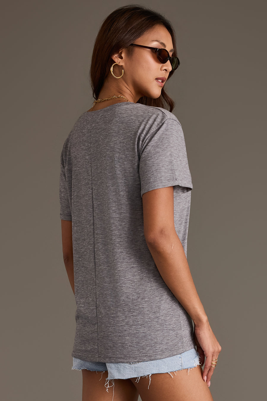 A person wearing a relaxed fit Gray Wine Tee with a center back seam and light-wash denim shorts.