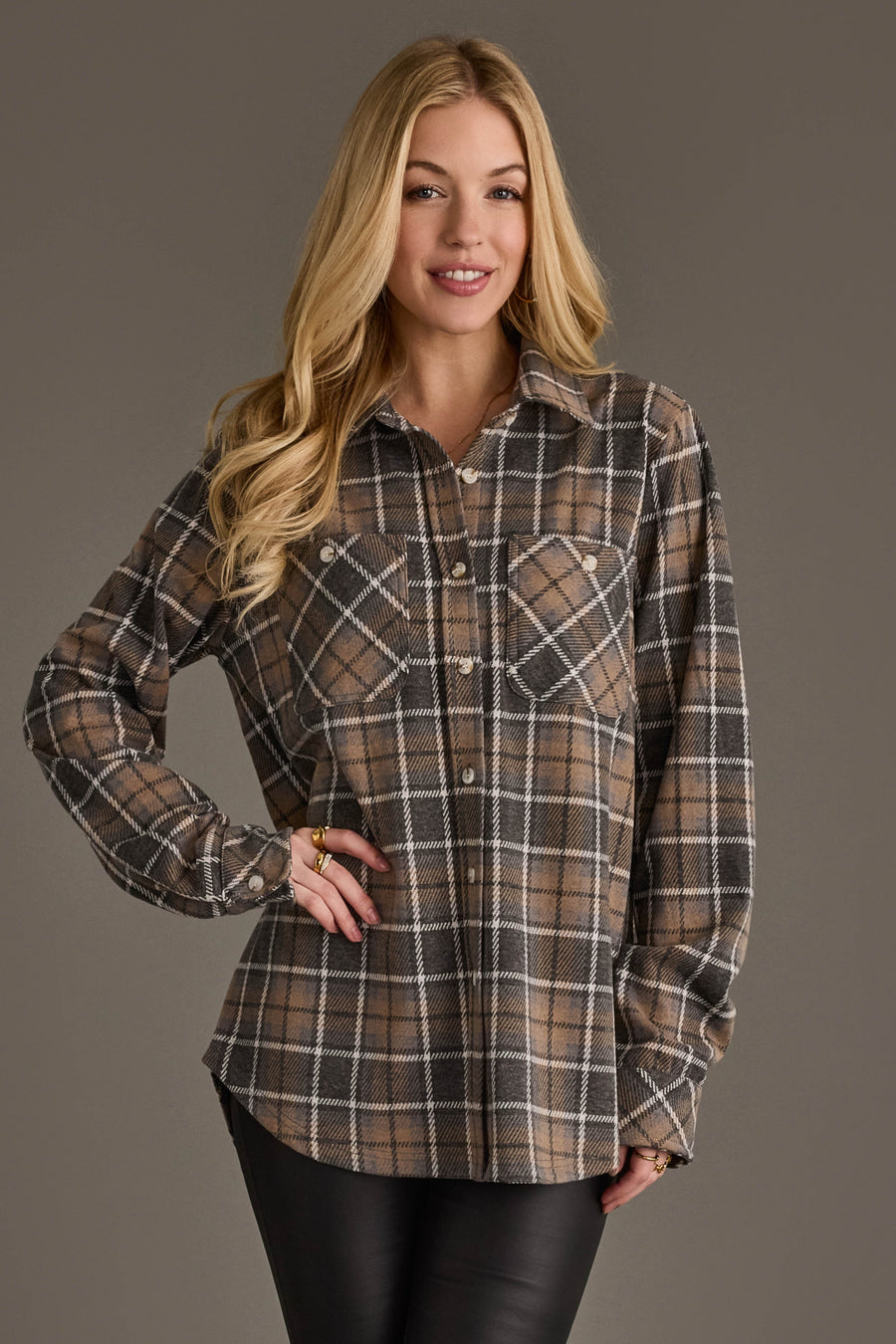 A woman with long blonde hair is wearing the Panache Apparel Collection’s Gray, Tan & White Plaid Button Up and black pants, standing with one hand on her hip and smiling against a plain background.