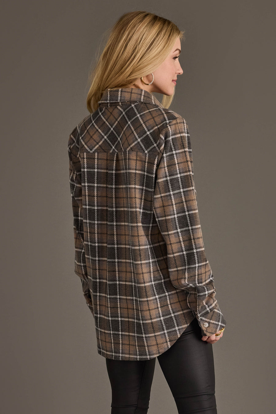 A woman with blonde hair, dressed in the Panache Apparel Collection’s Gray, Tan & White Plaid Button Up and black pants, stands facing away to display the back of the shirt.