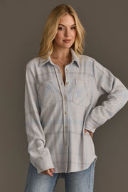 A person with long blonde hair wears the Panache Apparel Collection White, Gray & Light Blue Plaid Button Up, featuring front pockets, paired with light blue jeans. They stand against a plain taupe background with one hand on their hip and a slight smile.
