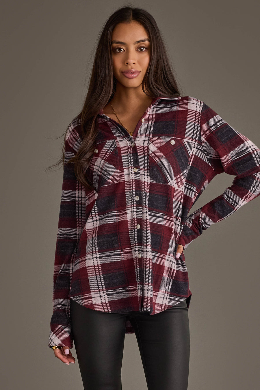 A woman stands against a gray background, wearing the Panache Apparel Collection’s Maroon, Charcoal & White Plaid Button Up with black pants, looking at the camera with a subtle smile.