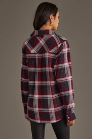 A woman with long brown hair, wearing the Panache Apparel Collection’s Maroon, Charcoal & White Plaid Button Up and black pants, stands facing away against a plain background.