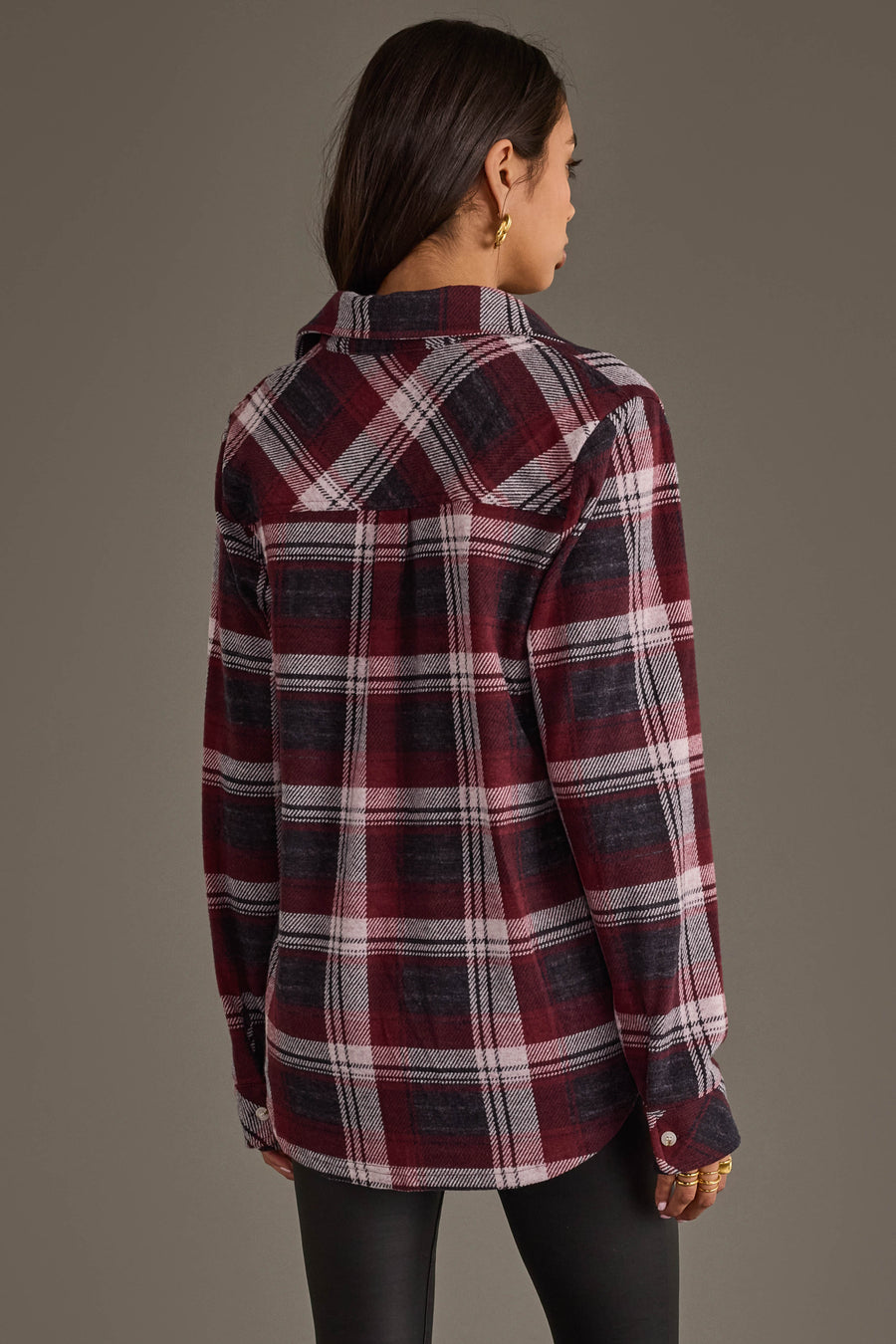 A woman with long brown hair, wearing the Panache Apparel Collection’s Maroon, Charcoal & White Plaid Button Up and black pants, stands facing away against a plain background.