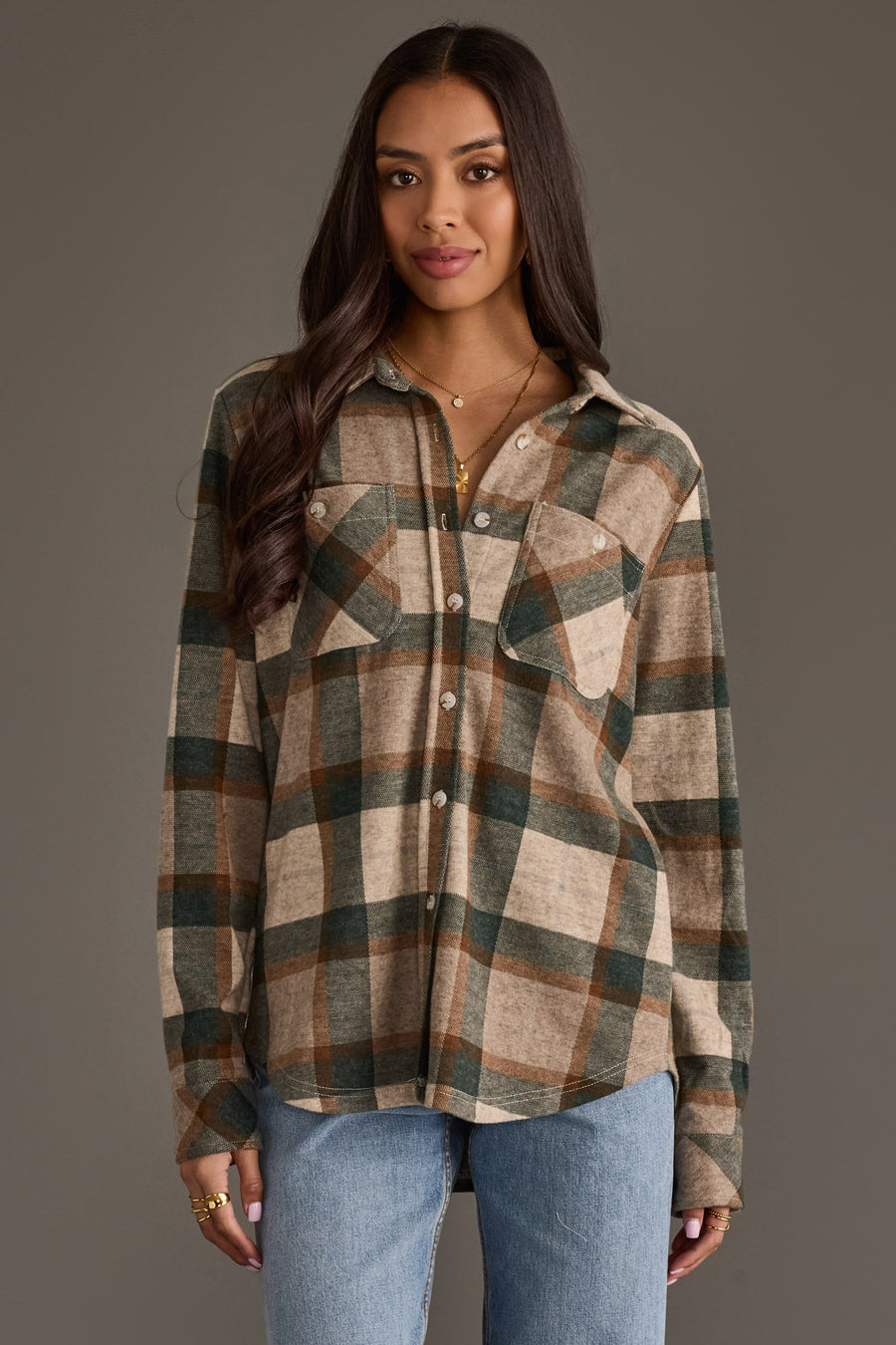 A woman wearing the Panache Apparel Collection’s Tan, Dark Green & Rust Plaid Button Up stands against a plain gray background in light blue jeans, looking at the camera with a slight smile.