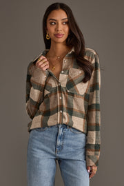A woman stands against a plain gray background, wearing the Panache Apparel Collection Tan, Dark Green & Rust Plaid Button Up shirt tucked into light blue jeans and accessorized with gold jewelry.