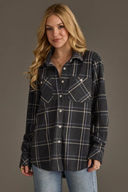 A woman with long blonde hair models the Panache Apparel Collection’s Dark Gray, Light Blue & White Plaid Button Up, pairing it with light blue jeans as she stands against a plain gray background and smiles slightly at the camera.