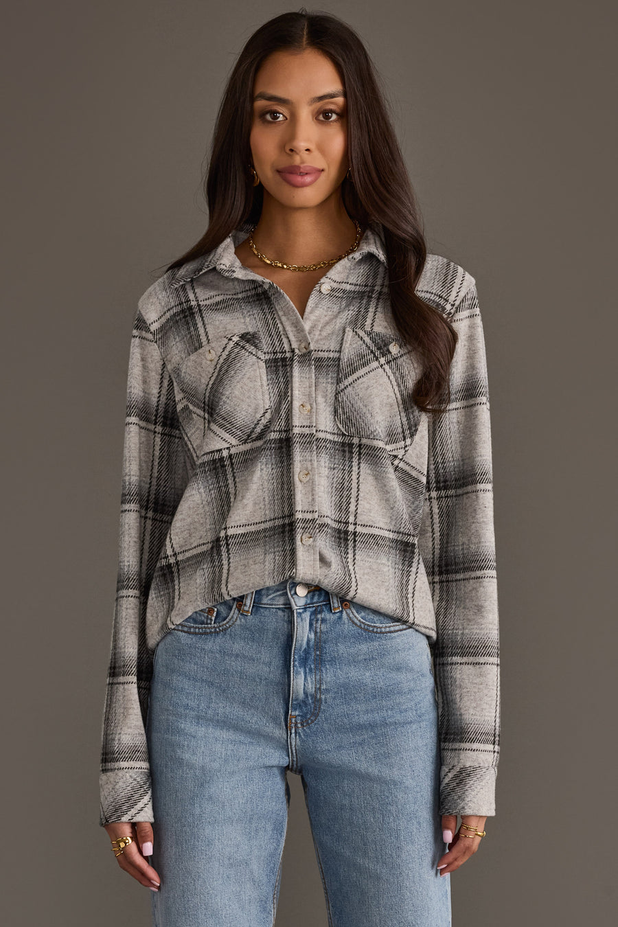 A woman wearing the Panache Apparel Collection Light Gray, Black & Sage Plaid Button Up with blue jeans stands against a plain gray background, looking at the camera with a neutral expression.