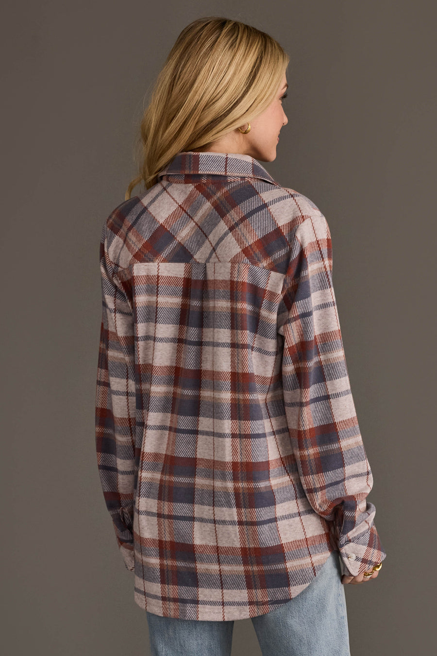 A person with long blonde hair, dressed in the Panache Apparel Collection Dusty Blue, Brick & Tan Plaid Button Up and light blue jeans, is facing away from the camera against a plain gray background.