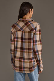 A woman with long brown hair, wearing large hoop earrings and blue jeans, stands facing away against a plain gray background while modeling the Dark Brown, Blue & Pink Plaid Button Up from Panache Apparel Collection.