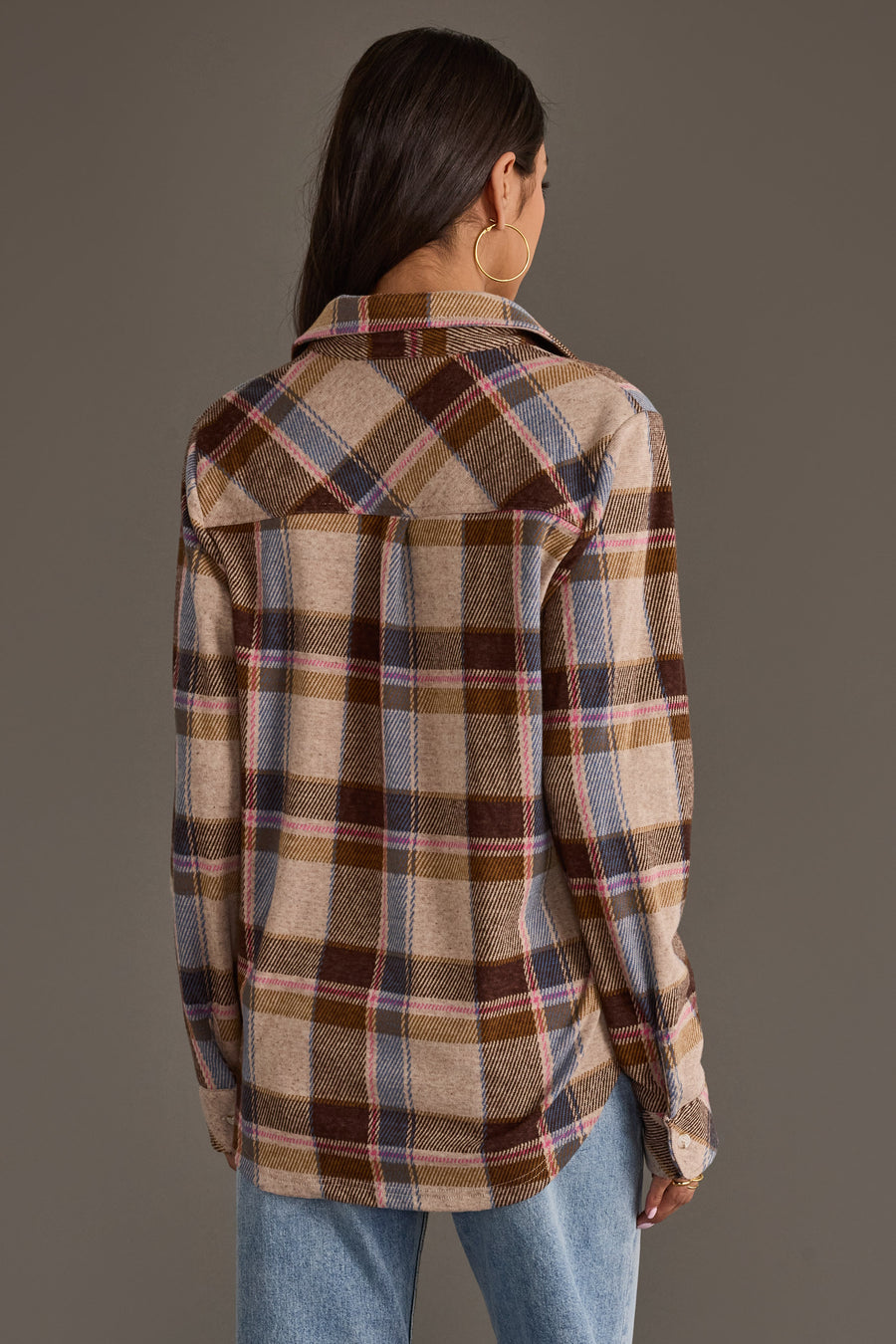 A woman with long brown hair, wearing large hoop earrings and blue jeans, stands facing away against a plain gray background while modeling the Dark Brown, Blue & Pink Plaid Button Up from Panache Apparel Collection.