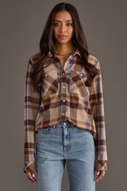 A woman with long brown hair wears the Panache Apparel Collection’s Dark Brown, Blue & Pink Plaid Button Up shirt and light blue jeans, standing against a plain gray background.