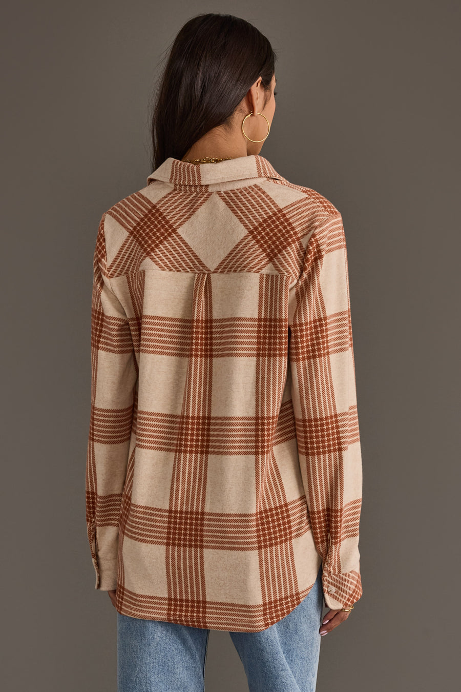 A woman with long dark hair, shown from the back against a plain gray background, wears the Panache Apparel Collection Cream & Rust Plaid Button Up paired with blue jeans.