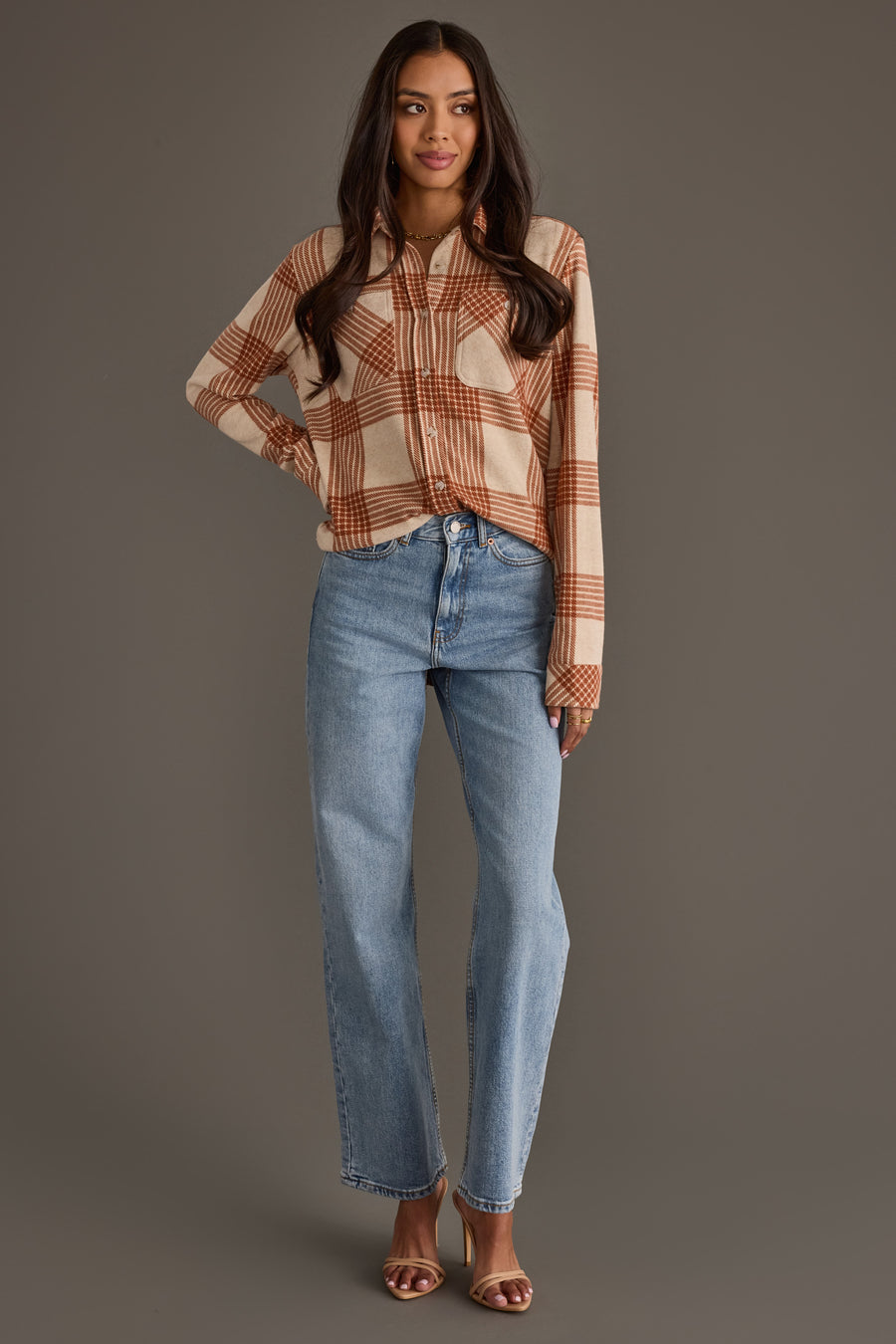 A woman stands against a plain background wearing the Panache Apparel Collection Cream & Rust Plaid Button Up, paired with light blue high-waisted jeans and brown heeled sandals.