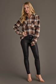 A woman stands smiling against a plain gray background, wearing the Panache Apparel Collection Brown, Black & Cream Plaid Button Up, paired with black leather pants and nude heels.