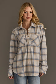 A woman with long blonde hair wears the Panache Apparel Collection Cream, Dusty Blue & Tan Plaid Button Up and light blue jeans, standing against a plain gray background and smiling softly.