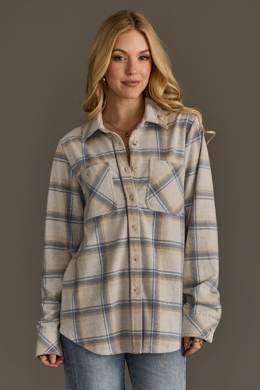 A woman with long blonde hair wears the Panache Apparel Collection Cream, Dusty Blue & Tan Plaid Button Up and light blue jeans, standing against a plain gray background and smiling softly.