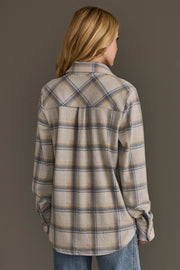 A person with blonde hair, seen from behind, wears the Panache Apparel Collection’s Cream, Dusty Blue & Tan Plaid Button Up and light blue jeans, standing against a plain gray background.