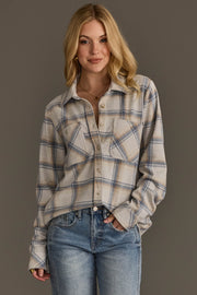 A person with long blonde hair wears the Cream, Dusty Blue & Tan Plaid Button Up from Panache Apparel Collection and light blue jeans, standing against a plain gray background and smiling with one hand in a pocket.