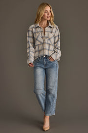 A woman stands against a gray background wearing the Panache Apparel Collection’s Cream, Dusty Blue & Tan Plaid Button Up, paired with light blue jeans and beige heels. She has medium-length blonde hair and gazes slightly to the side with a relaxed expression.