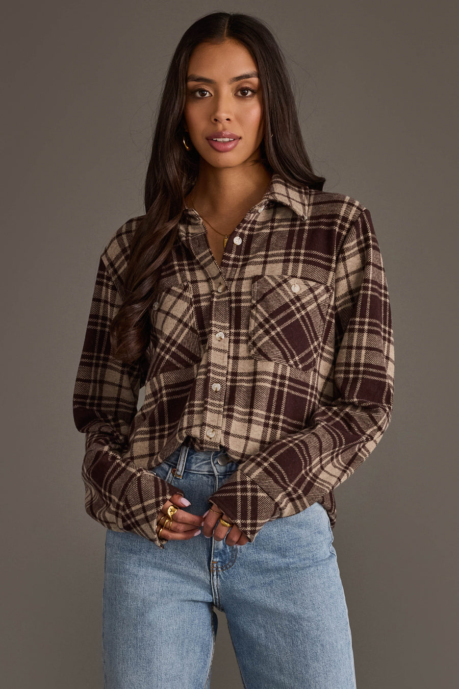 A woman wearing the Panache Apparel Collection Chocolate Brown & Tan Plaid Button Up and light blue jeans stands against a plain gray background, looking at the camera with a neutral expression.