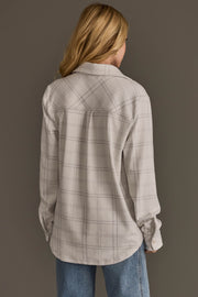 A person with long blonde hair, wearing the Panache Apparel Collection White & Light Gray Plaid Button Up and blue jeans, stands facing away from the camera against a plain gray background.
