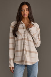 A woman with long brown hair wears the Panache Apparel Collection’s Cream, Tan & Gray Plaid Button Up paired with blue jeans, standing against a plain gray background.