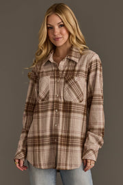 A woman with long blonde hair models the Panache Apparel Collection’s Brown, Tan & Rose Plaid Button Up, featuring pockets, paired with light blue jeans, standing against a plain gray background.