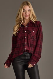 A woman with long blonde hair models the Panache Apparel Collection Maroon & Black Plaid Button Up, paired with black leather pants and set against a plain gray background.