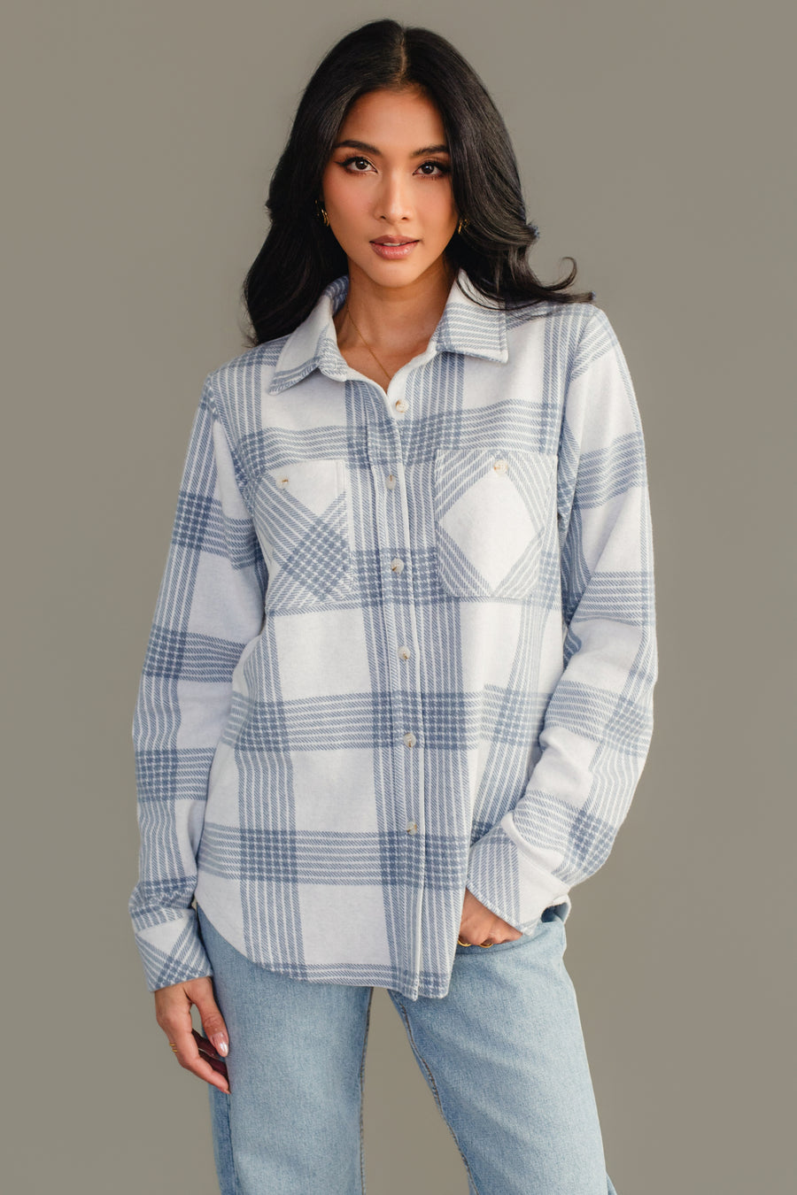 A woman wearing the Panache Apparel Collection White & Dusty Blue Plaid Button Up, featuring front pockets, paired with light blue jeans and standing against a plain gray background.