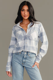 A woman with long dark hair is wearing the Panache Apparel Collection’s White & Dusty Blue Plaid Button Up paired with light blue jeans, standing against a plain gray background.