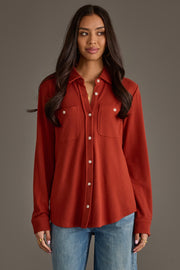 A woman wearing the Panache Apparel Collection Dark Rust Super Soft Button Up with front pockets and blue jeans stands against a plain gray background.